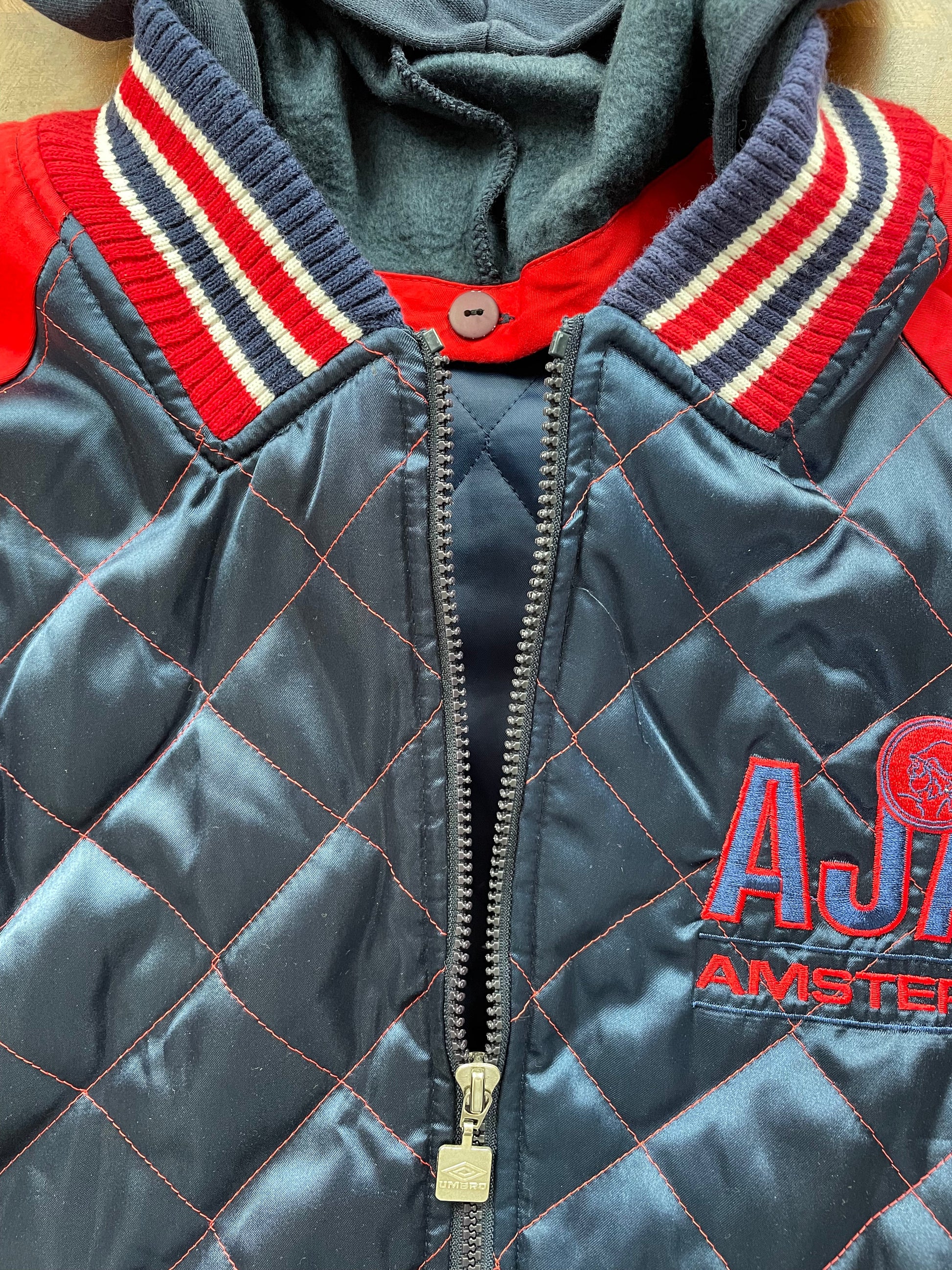 A vintage-style quilted jacket displayed on a mannequin torso. The jacket features a navy blue diamond-quilted body with red and white striped ribbed collar
