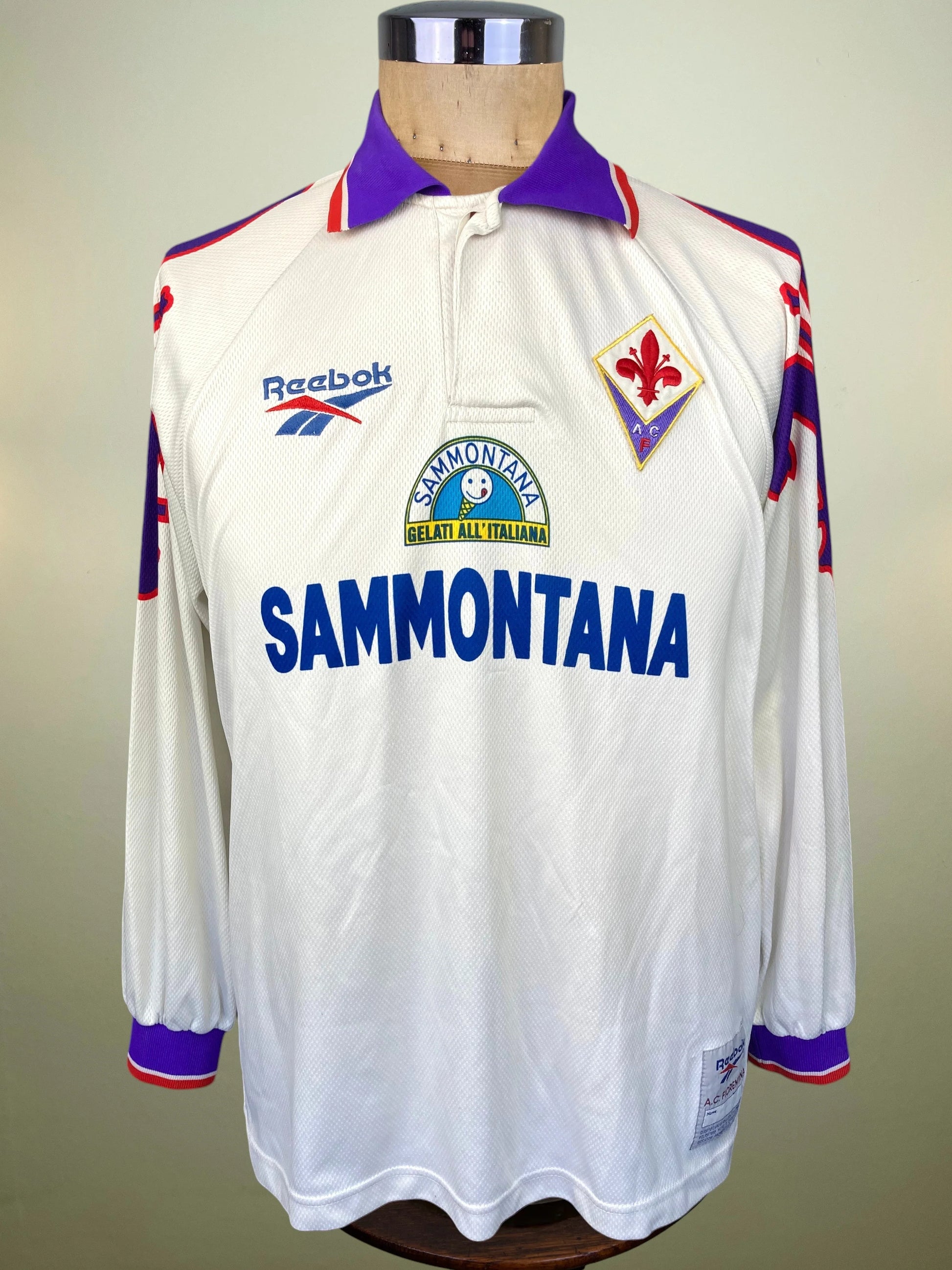 A vintage long-sleeve Reebok football jersey displayed on a mannequin torso. The white jersey features a purple collar