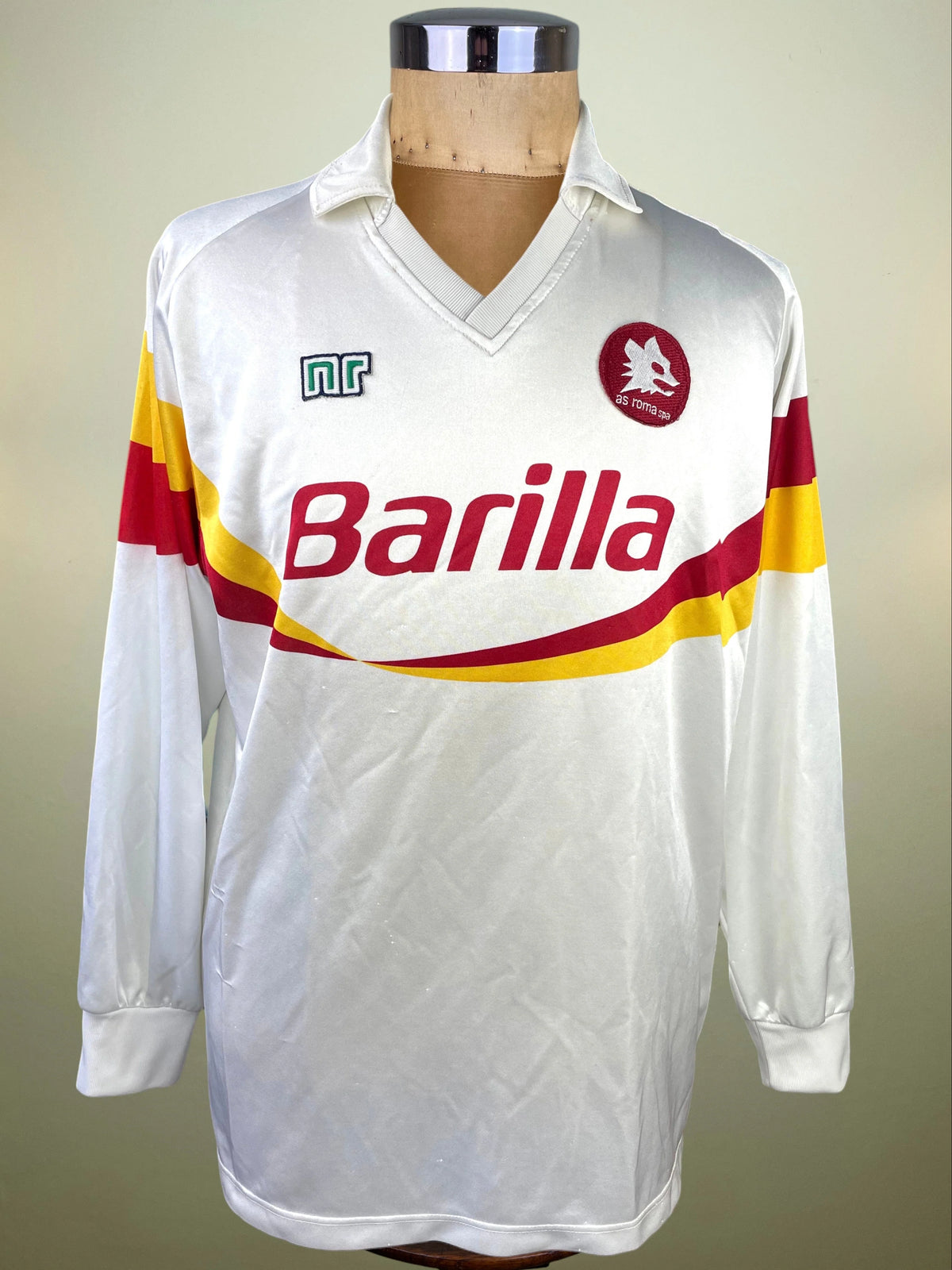A vintage long-sleeve white soccer jersey displayed on a wooden mannequin torso. The jersey features the red and yellow striped logo of Barilla across the chest