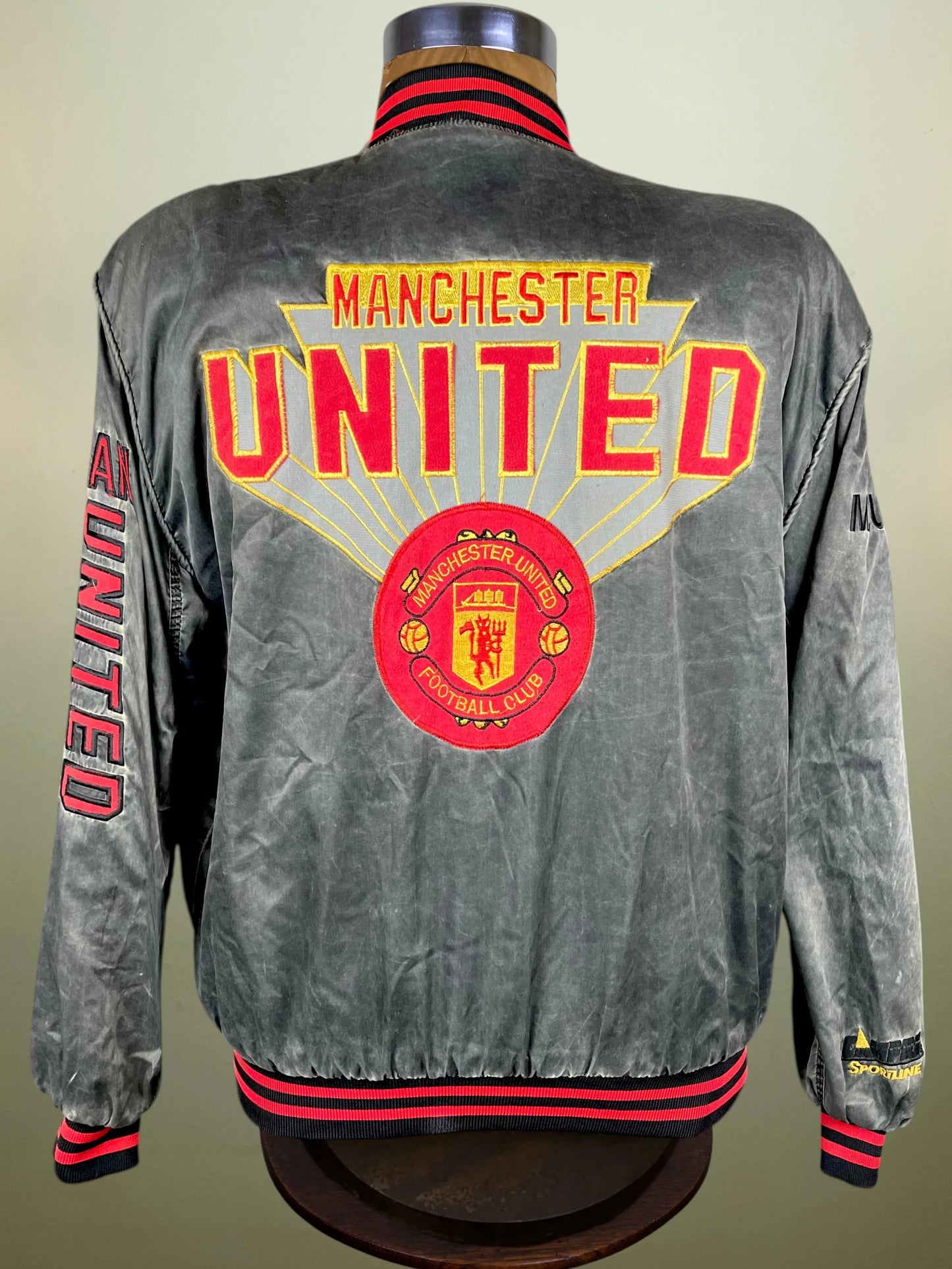 A gray satin Manchester United bomber jacket displayed on a mannequin