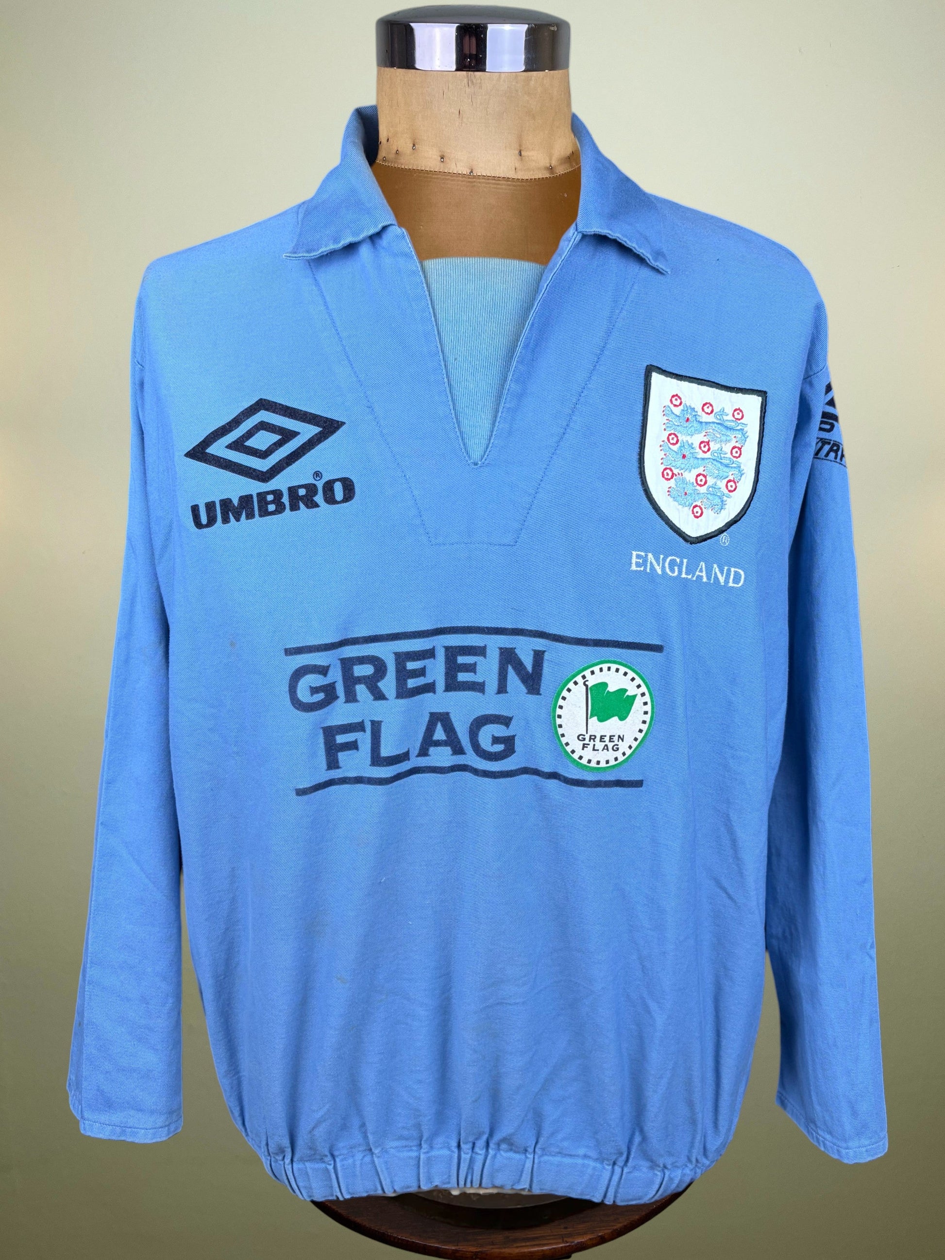 A light blue long-sleeve England soccer jersey displayed on a mannequin torso. The jersey features the Umbro logo on the right chest