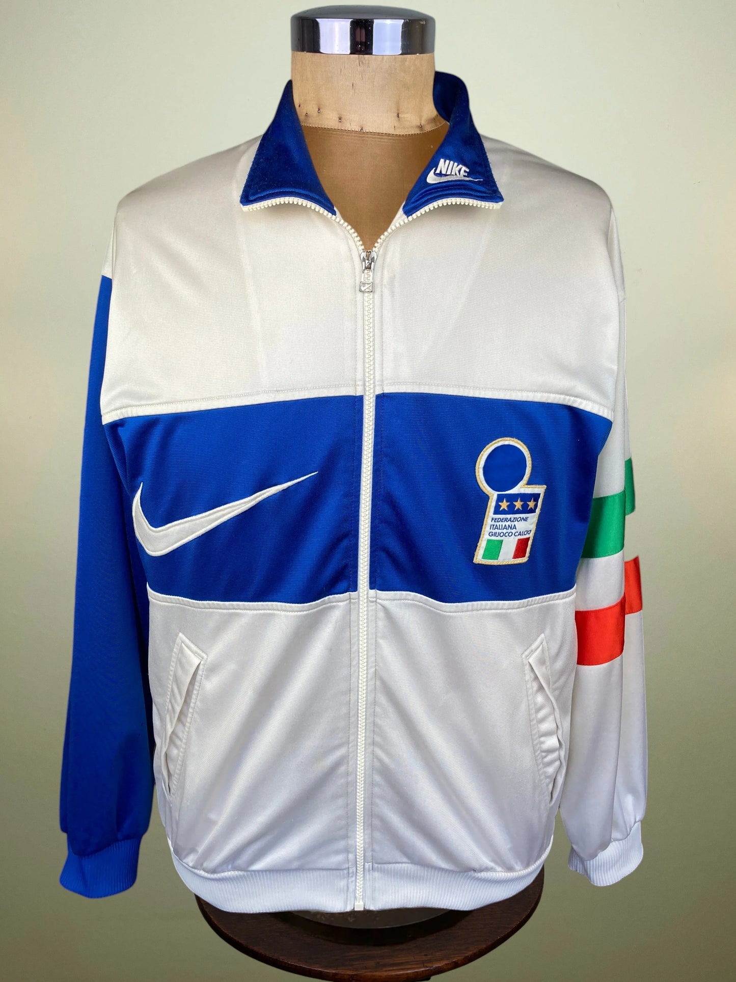 A vintage Nike track jacket displayed on a mannequin torso. The jacket is white with royal blue panels on the chest and sleeves
