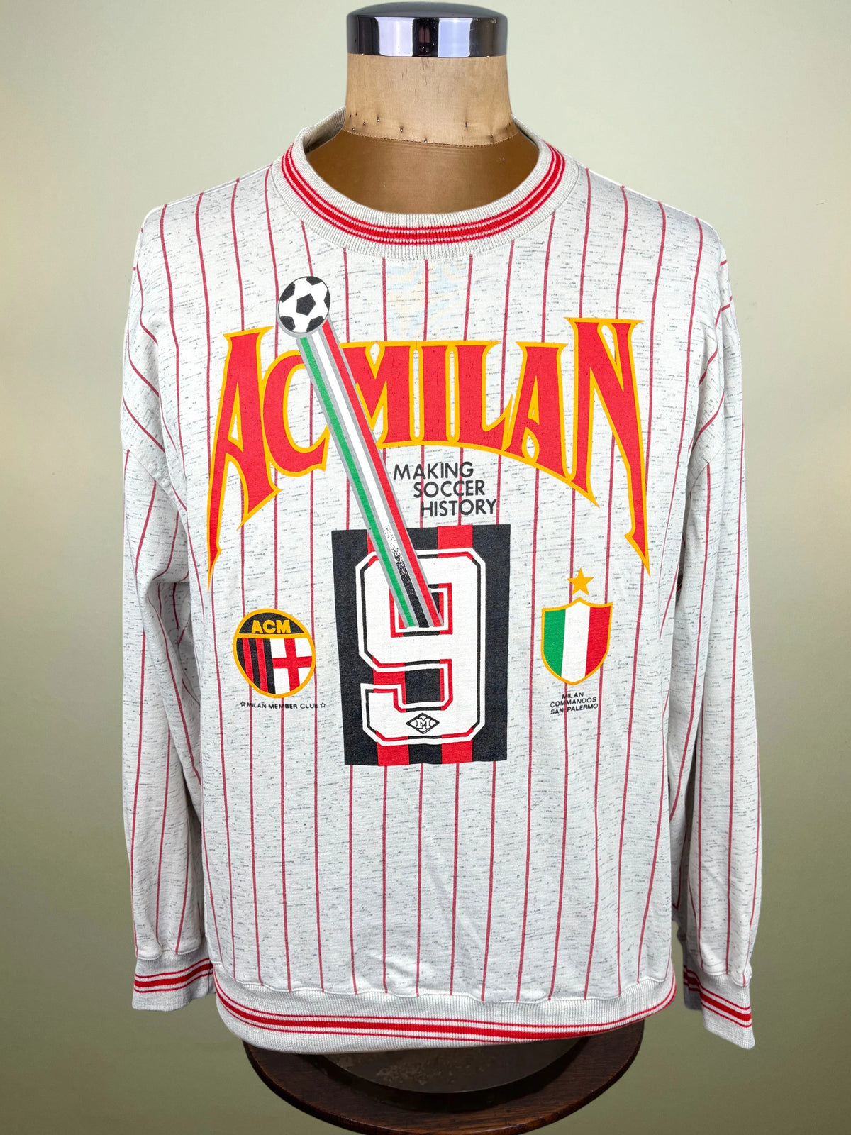 A long-sleeve AC Milan soccer jersey displayed on a mannequin torso. The jersey is light gray with thin red pinstripes and features a large front graphic with 'AC MILAN' in orange-red