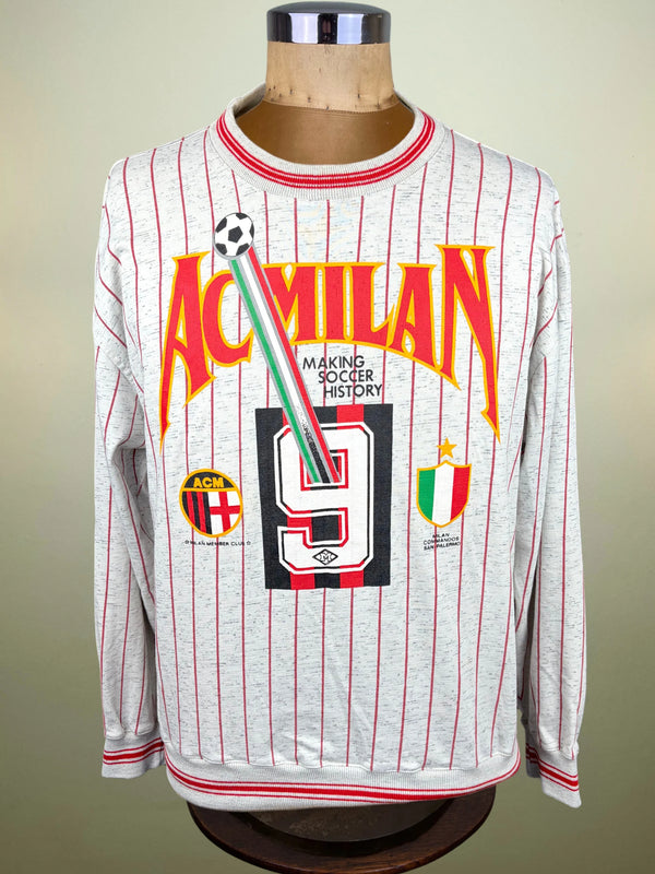 A long-sleeve AC Milan soccer jersey displayed on a mannequin torso. The jersey is light gray with thin red pinstripes and features a large front graphic with 'AC MILAN' in orange-red